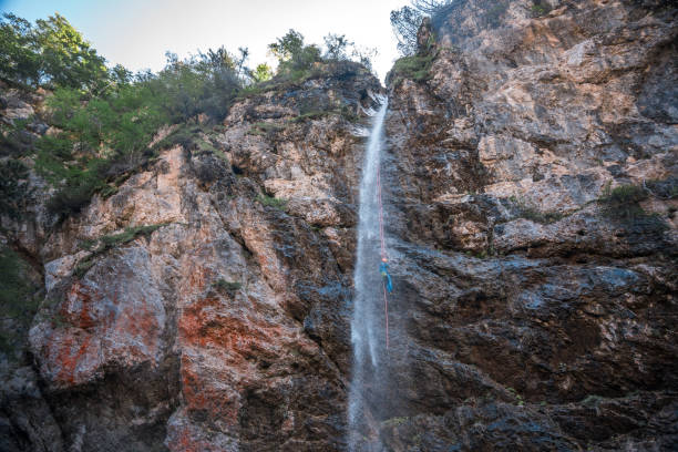 An individual in a neoprene suit and safety helmet, descending a waterfall with a rappel rope during an exciting canyoning adventure.