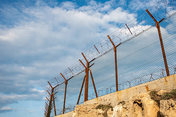 istock Security fence with barbed wire against a blue cloudy sky. Security border forbidden access 2204238156