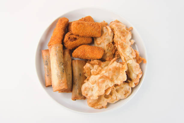 A delicious assortment of deep-fried snacks featuring spring rolls, fritters, and crunchy bites served on a white plate. Such as Fried Banana, Piscok, and Risol mayo