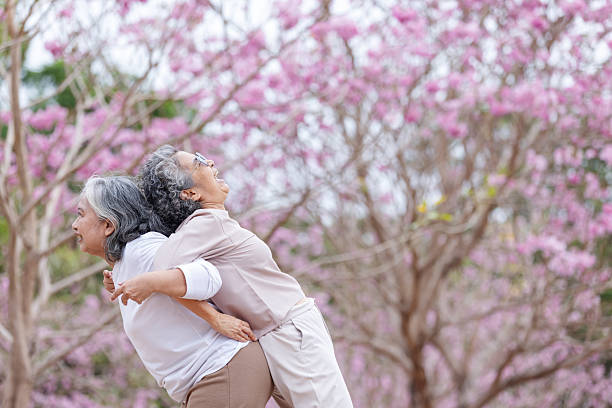 istock Two elderly women share a joyful moment, laughing and embracing under blooming cherry blossoms. 2204255602