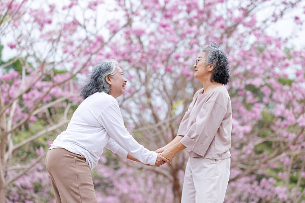 istock Two elderly women share a heartfelt moment under cherry blossoms, holding hands and laughing together. 2204255672