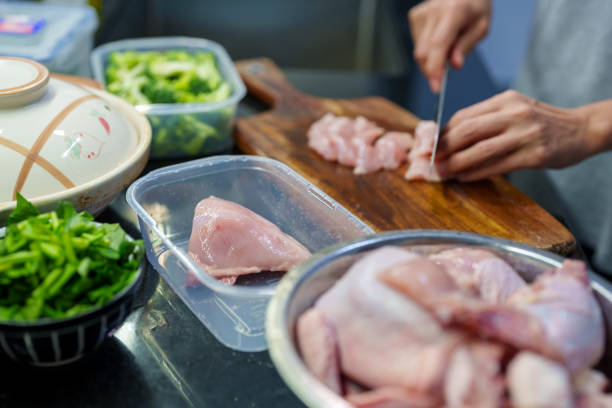 A person cutting chicken breast on a wooden board, preparing fresh ingredients with reusable food containers, promoting sustainable cooking and zero-waste meal planning at home.