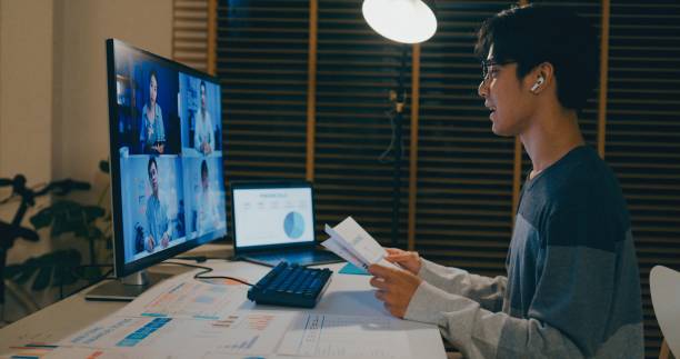 istock Young Asian video conference late at night from home office, financial documents and discussing with colleagues online, showcasing remote teamwork and dedication. Remotely and finance. 2204263682