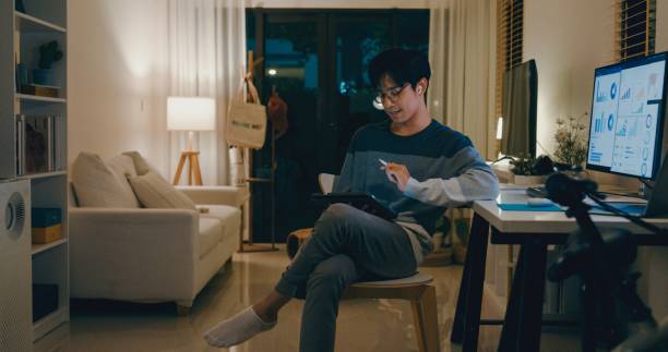 istock Young Asian man financial advisor working late at home, using a tablet and laptop, discussing strategy with clients via video call, showcasing remote work efficiency. Remotely and finance. 2204263693
