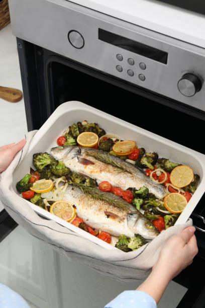 istock Woman taking baking dish with delicious fish and vegetables from oven, closeup 2204265420