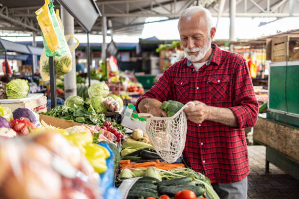 istock Senior man buying broccoli at a farmer's market using reusable bag 2204265525