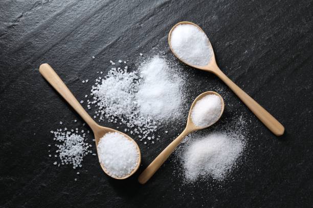istock Organic salt in spoons on black table, flat lay 2204268641