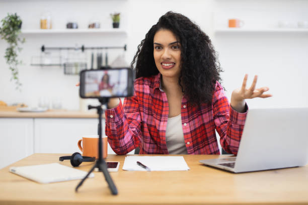 istock Young woman recording vlog at home using smartphone and laptop 2204271270