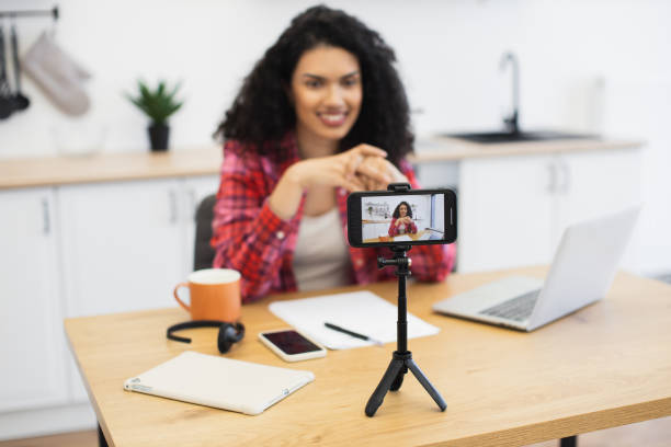 istock Young woman recording video blog in modern kitchen using smartphone setup 2204271291