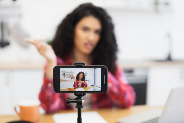 Woman recording a video in kitchen using smartphone on tripod setup