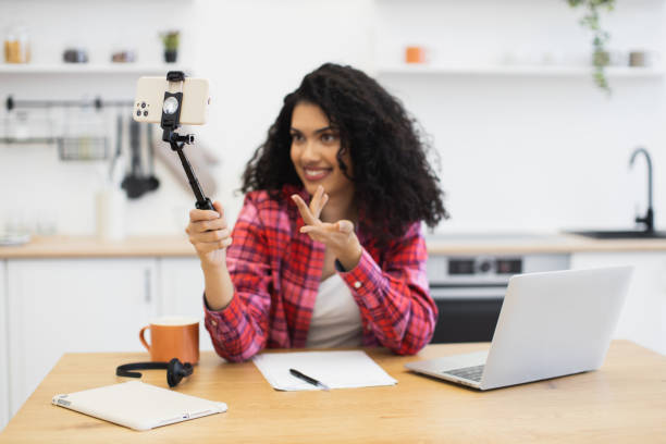 istock Young African woman filming vlog in kitchen using smartphone and tripod 2204271309