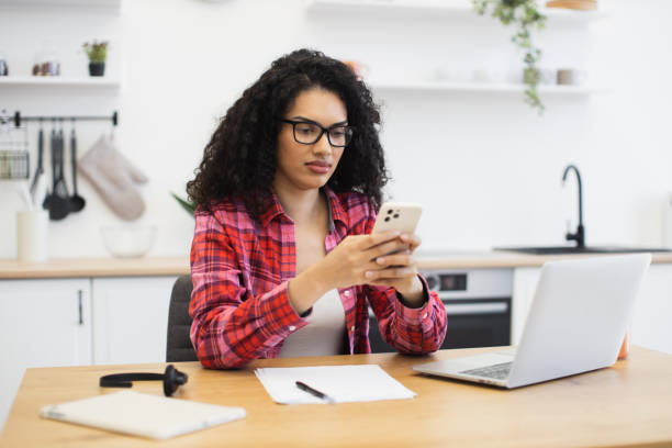 istock Young woman in kitchen multitasking with smartphone and laptop computer 2204271325