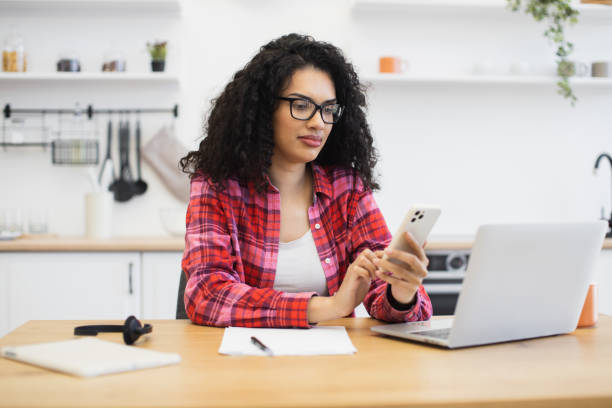 istock Young woman using smartphone at home while working remotely on a laptop 2204271336