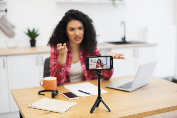 istock Young woman recording video at home using smartphone and tripod 2204271337