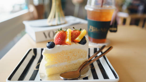 A slice of fruit-topped cake on a striped plate with a refreshing drink, set in a cozy cafe atmosphere.