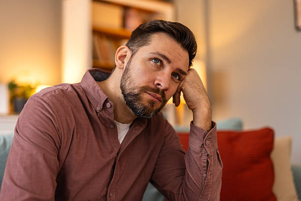 istock A man sits on a couch with a thoughtful expression. The scene has a relaxed atmosphere with soft lighting and a modern interior. Concept of deep thinking, decision-making, or introspection. 2204276080