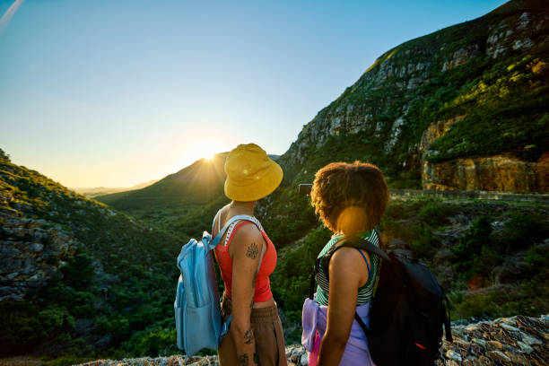Two young women hikers with backpacks enjoying a scenic sunset view in a mountain valley during their adventure