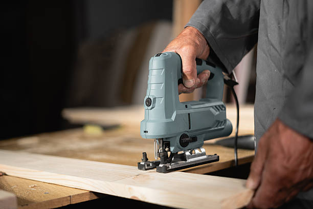 Carpenter sawing wooden plank with electric jigsaw in carpentry workshop
