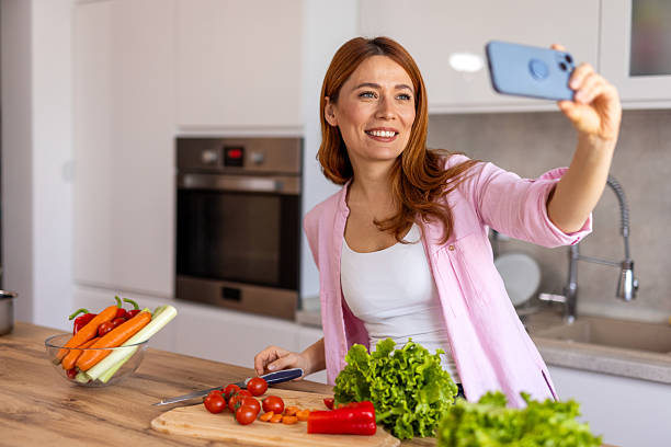 istock A woman in a modern kitchen prepares dinner while taking a selfie, capturing a fun and joyful moment. She is multitasking, cooking a delicious homemade meal while enjoying the process. 2204277253