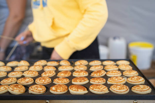 Making mini pancakes on the pancake machine. Typical Dutch poffertjes - tiny pancakes-being baked on a heavy cast iron pan being prepared during street food festival, an outdoor event. Dutch small, fluffy pancakes, made on hot cast iron plate.