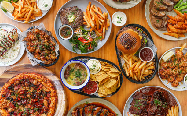 Table top of variety of assorted dishes of pizzas, burgers, fries, sauces and other delicious items.
