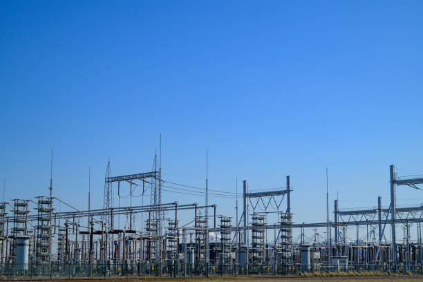 High-voltage power lines at an electricity distribution substation with high voltage electric transmission towers under a blue sky.
