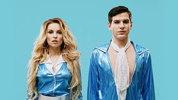A captivating image shows two individuals in vibrant blue outfits posing against a stunning teal backdrop