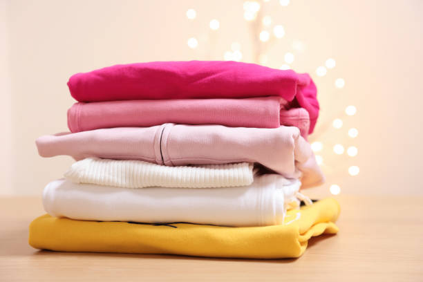 istock Stack of folded clothes on wooden table against beige background with blurred lights 2204286540