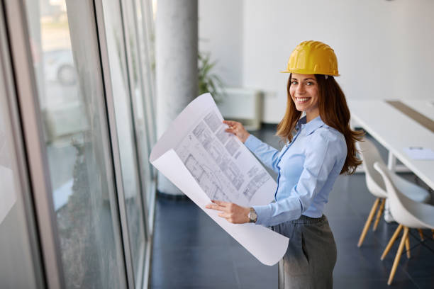 istock Smiling female architect reviewing blueprints in modern office 2204288179