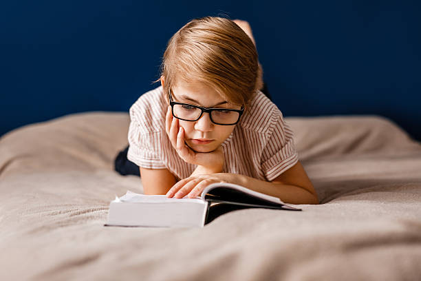 istock A 10-year-old boy with glasses is lying on the bed reading a big book 2204289548