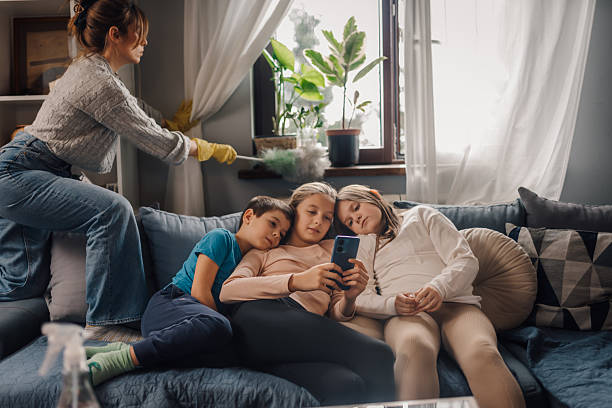 istock Mother dusting while children relaxing on sofa with smartphone 2204290050