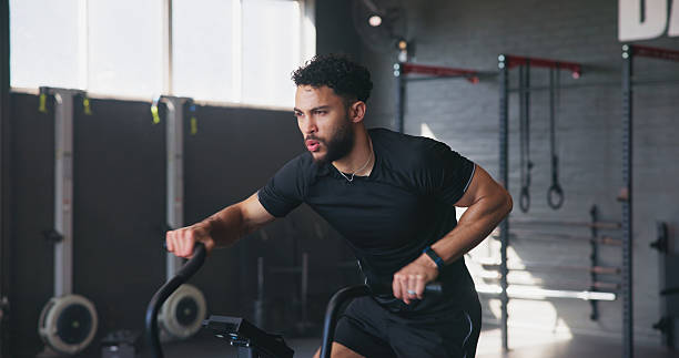 istock Fitness, man and bicycle machine in gym for exercise, cardio workout and training. Athlete, stationary bike and breathing in wellness center for triathlon preparation, intense cycling and aerobics 2204301366