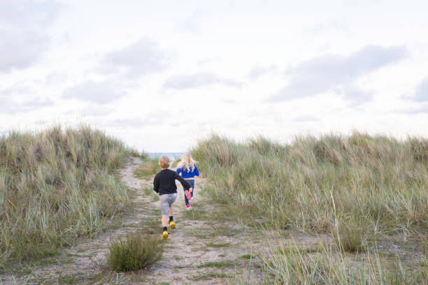istock Children running on sand dune towards the sea. 2204307231