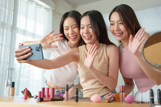 istock Three Young Pretty Asian friends happily pose and take selfies with smartphone together while exploring makeup products in a room with cosmetic items. 2204314991