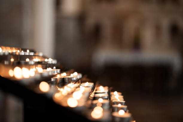 A row of lit prayer candles glowing in a dimly lit church, symbolizing faith, remembrance, hope, and spiritual devotion.