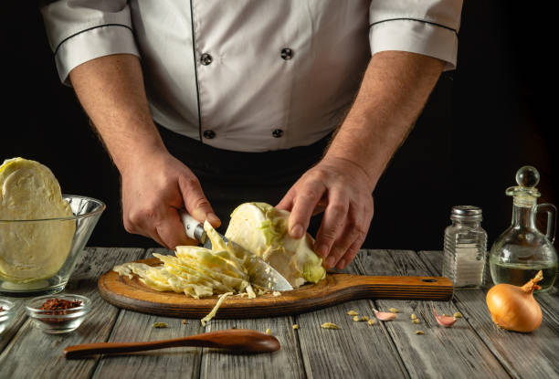 istock A chef dressed in a white uniform meticulously slices fresh cabbage on a rustic wooden board. Nearby ingredients like onions, oil, and spices create an inviting atmosphere in the kitchen 2204316973