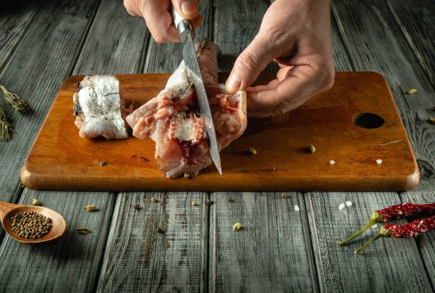 istock In a cozy kitchen, a skilled chef carefully cuts raw hake on a weathered wooden cutting board. Spices and herbs are scattered throughout, evoking a sense of culinary creativity and tradition 2204316991
