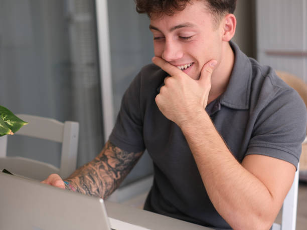 istock Young handsome tattooed caucasian guy concentrated on his smartphone while working or studying on laptop at home 2204322127