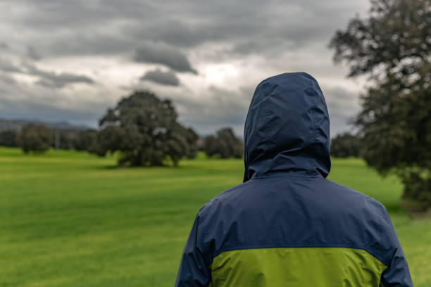 Villamantilla, Madrid, Spain. Farmer looking at a green field of cereal in winter, wearing a raincoat under a cloudy sky