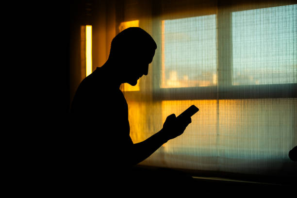 istock Silhouette of a man using smartphone near window at sunset 2204323884