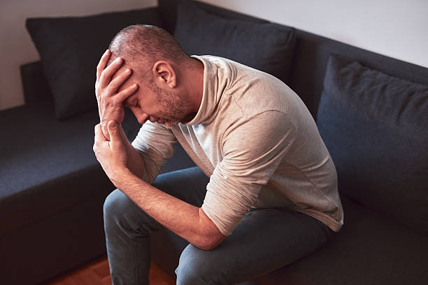 istock Man with headache and depression sitting on a sofa at home. 2204330214