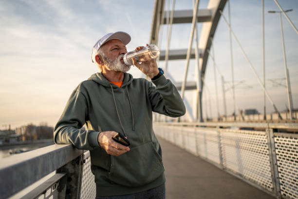 istock Senior man drinking water after exercising on a bridge 2204339789