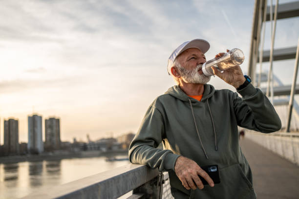 istock Senior man drinking water after exercising on bridge at sunset 2204339808