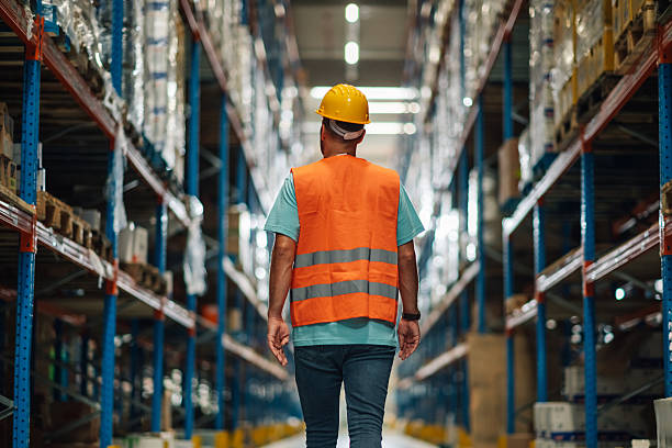 istock Warehouse worker walking through large distribution warehouse with shelves full of goods 2204342426