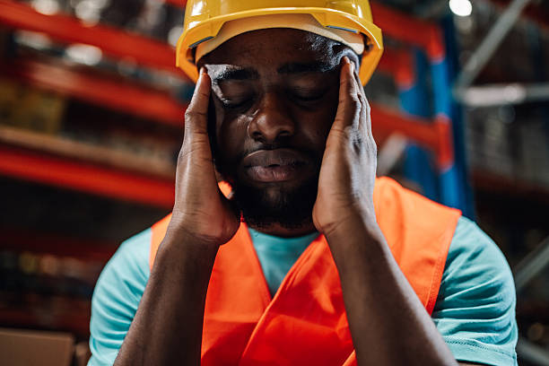 Tired black warehouse worker suffering from headache in a storage room