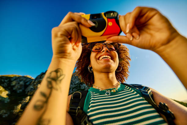 Smiling female hiker taking pictures of the landscape with a disposable camera during a sunny day in the mountains