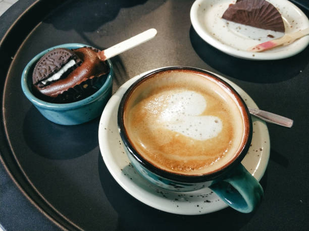 A delicious cup of coffee topped with a heart shape foam is placed alongside a chocolate dessert on a tray in a welcoming cafe atmosphere.