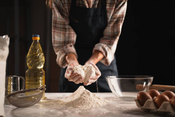 istock Unrecognizable female baker in apron working with flour on table, preparing dough for bread and sweet pastries. Cozy atmosphere of baking at home, focus on hands 2204347590