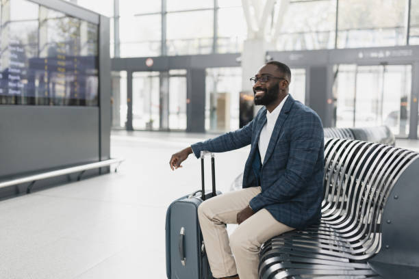 A cheerful man in a blazer sits at the airport, ready for travel. His stylish attire and bright smile convey excitement for his upcoming journey.