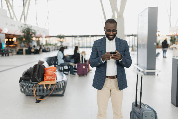 istock Smiling man using smartphone at busy airport terminal 2204350272